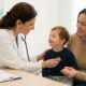 "Foto de una pediatra examinando suavemente el corazón de un niño de 4 años con síndrome de Down con un estetoscopio, mientras su madre lo reconforta. El niño sonríe. Es una escena de atención médica pediátrica preventiva en una clínica moderna con un cartel de 'SEGUIMIENTO INTEGRAL'. En primer plano, una carpeta dice 'Cita de Salud - Jupsin.com' para la salud en igualdad."